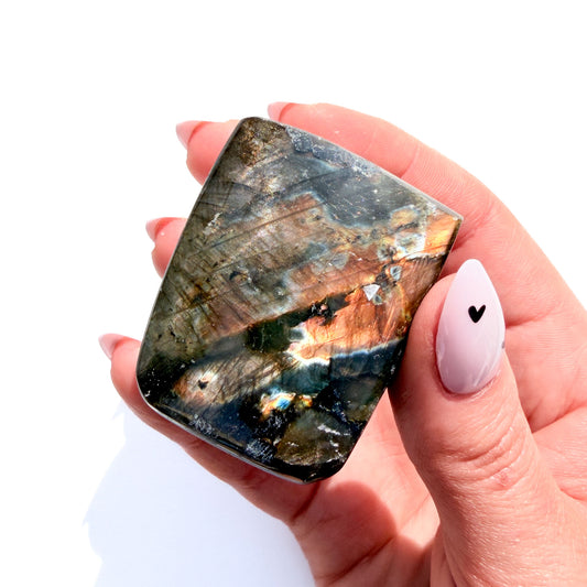 labradorite freeform crystal freeform with flash, on a white background, in hand.