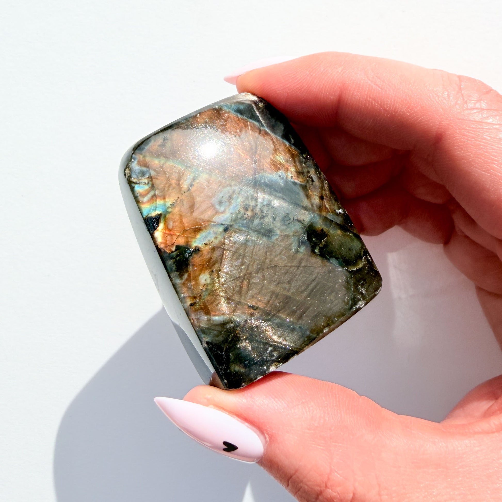 labradorite freeform crystal freeform with flash, on a white background, in hand.