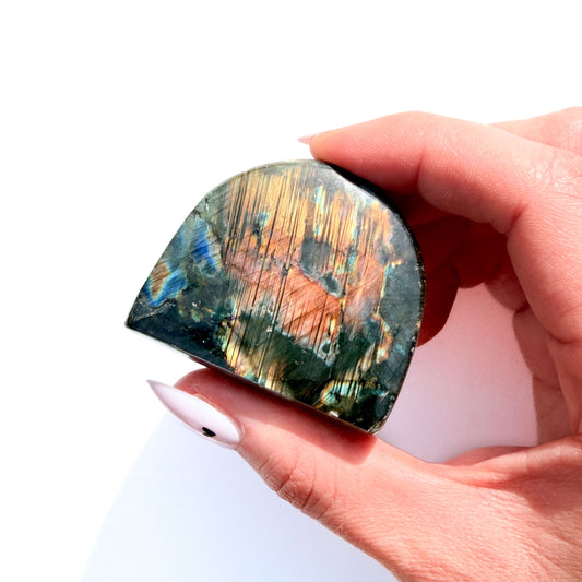 labradorite freeform crystal freeform with flash, on a white background, in hand.